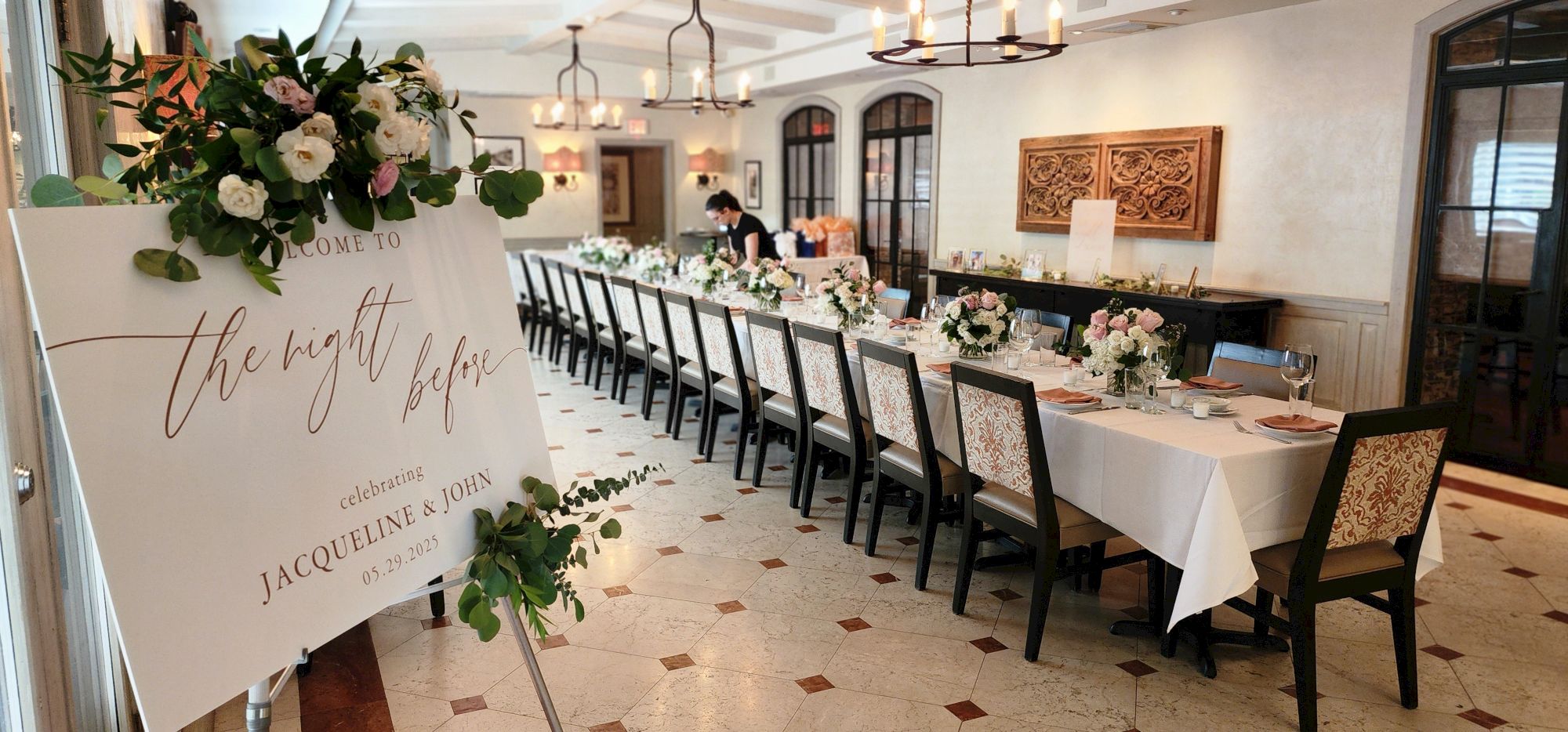 The image shows a long dining table set for an event, with a welcome sign that says “the night before” for Jacqueline and John.
