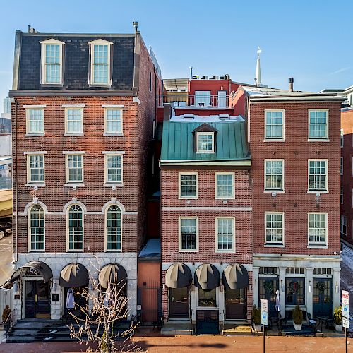 Colorful row of brick townhouses with arched shop fronts on ground level, narrow windows, and a bright blue sky above.
