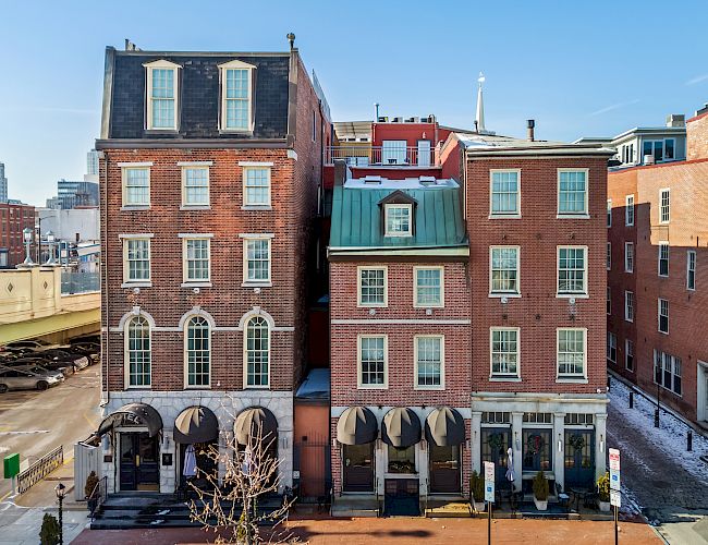 Colorful row of brick townhouses with arched shop fronts on ground level, narrow windows, and a bright blue sky above.