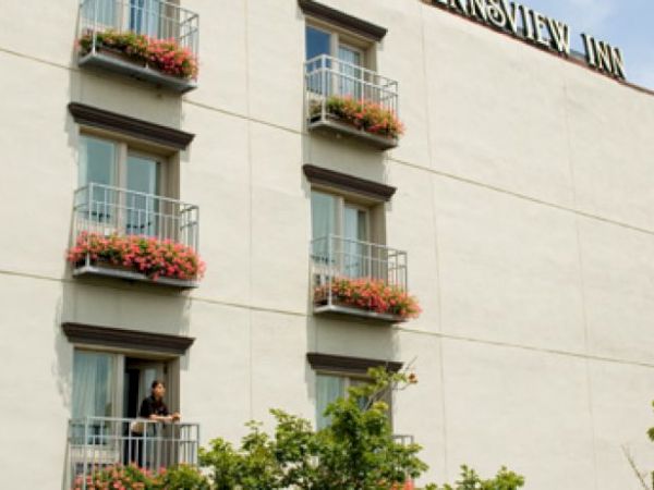 A beige building with balconies and flowers, titled "RIVERVIEW INN," near a large bridge under a blue sky.