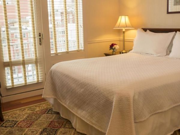 A cozy bedroom with a double bed, white bedding, armchair, table lamp, and window with shutters, creating a warm ambiance.