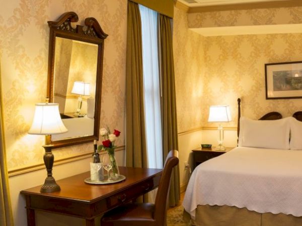 A cozy hotel room featuring a double bed, nightstands with lamps, a mirror, and a table with chairs. The decor is classic and elegant.