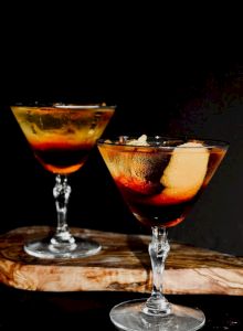 Two cocktails in coupe glasses with orange slices, dark background, a festive, tropical vibe.