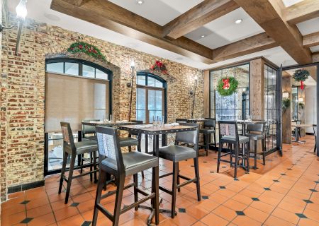 A stylish restaurant or cafe with brick walls, arched windows, wooden benches and high tables, tiled floor, and hanging greenery decor.