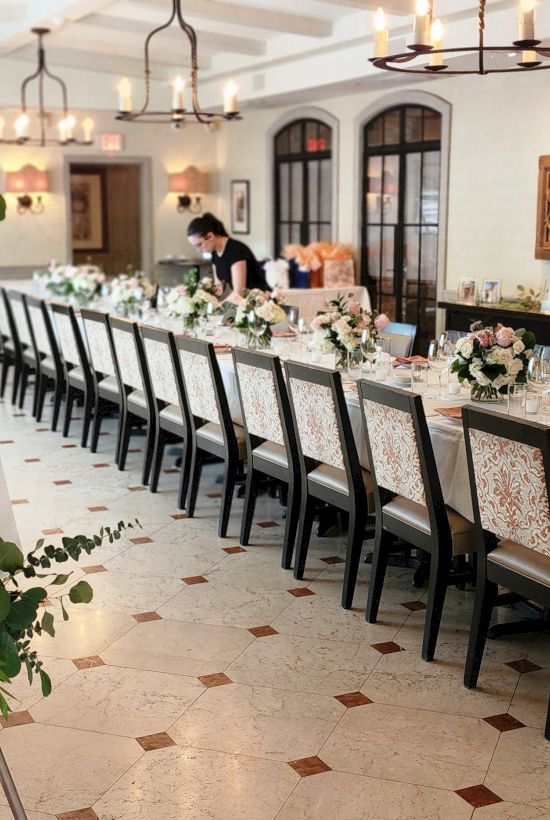 A decorated table setup for an event with floral arrangements, featuring a sign that reads "Welcome to The Night Before" in a dining area.