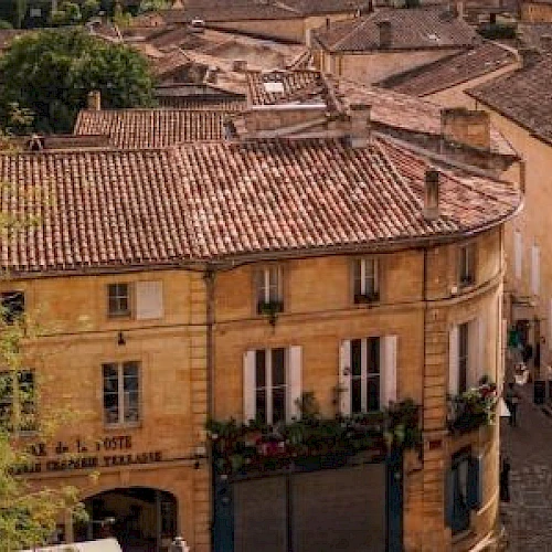 Aerial view of a charming European town with rustic buildings, red-tiled roofs, and cobblestone streets, surrounded by lush greenery.