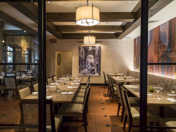 A cozy restaurant dining area with wooden tables and chairs, elegant lighting, and artwork on the walls, ready for guests.