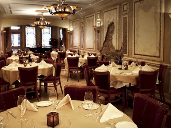 The image shows an elegant restaurant interior with round tables set with white napkins, wine glasses, and ornate decor on the walls.