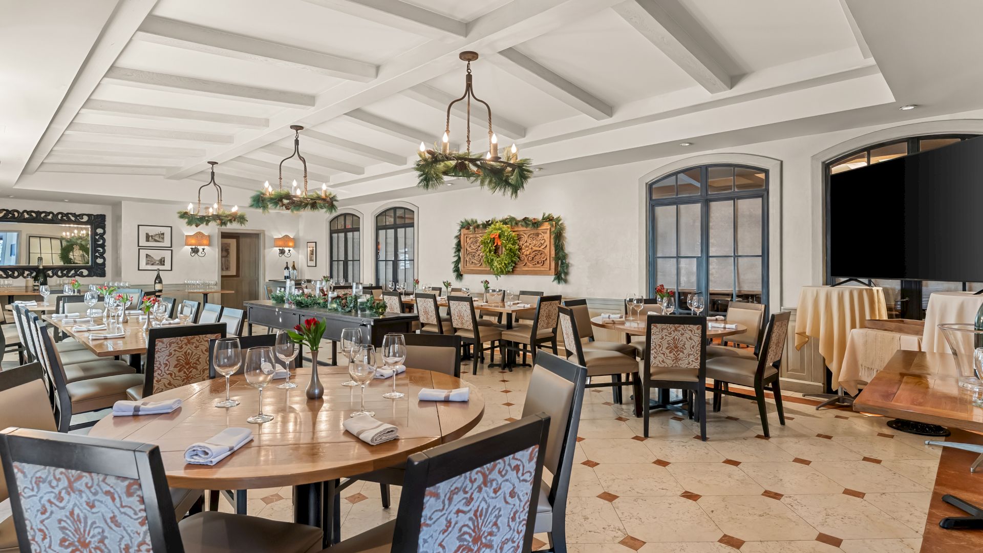 A elegant dining room with round tables, upholstered chairs, chandeliers, and a warm, classical decor; windows and buffet area visible.