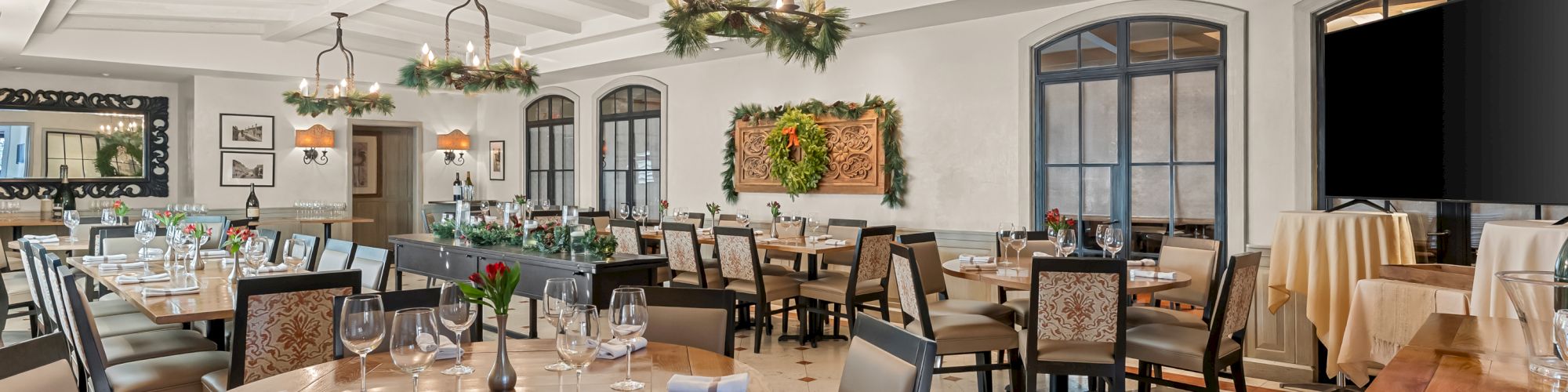 A elegant dining room with round tables, upholstered chairs, chandeliers, and a warm, classical decor; windows and buffet area visible.