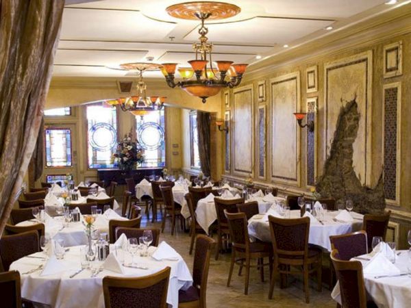 A sophisticated restaurant interior featuring elegantly set tables, chandeliers, and ornate wall decor, creating a refined dining atmosphere.
