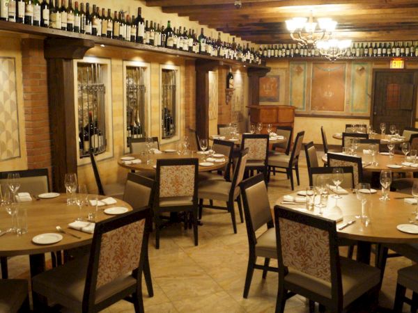 A cozy restaurant interior with wooden tables, chairs, and wine bottles lining the walls, elegantly set for dining.