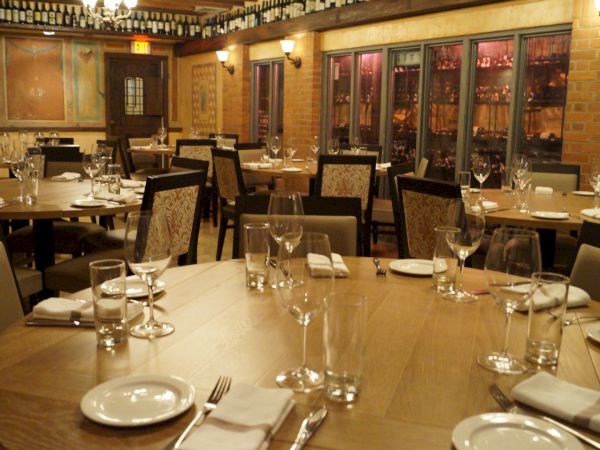 The image shows an elegant restaurant interior with neatly set tables, wine glasses, and decorative bottles on display shelves.