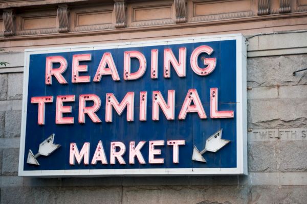 A sign for "Reading Terminal Market" on a wall, featuring red neon letters on a blue background, with decorative arrows included.
