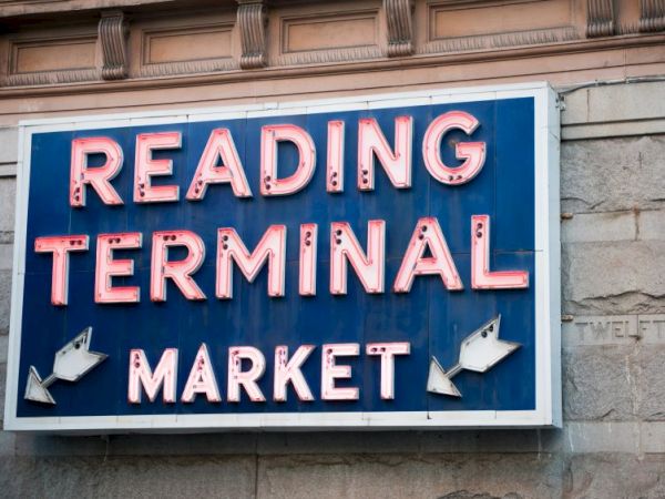 A sign for "Reading Terminal Market" on a wall, featuring red neon letters on a blue background, with decorative arrows included.