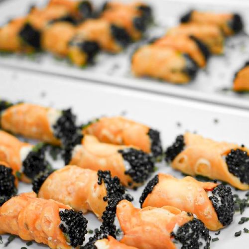Pastry shells filled with cream and topped with black caviar are arranged on white plates.