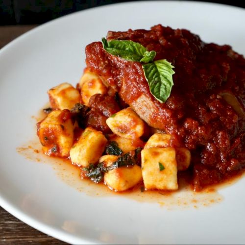 The image shows a plate of gnocchi with tomato sauce and garnished with a sprig of mint on a white plate.