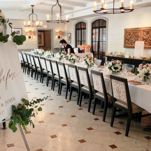 Elegant dining room set for an event, with a sign titled “The Night Before” and floral arrangements on a long table.