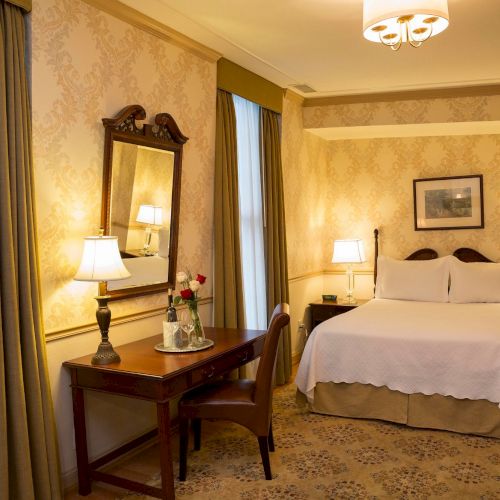 A cozy, well-lit hotel room with a double bed, a table with chairs, lamps, and elegant decor.