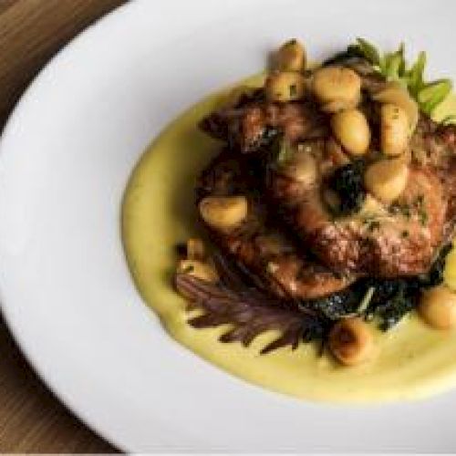 A plated dish featuring roasted chicken, greens, garlic cloves, and yellow sauce on a white plate.