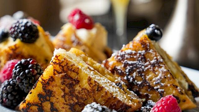 French toast topped with berries and powdered sugar on a plate, alongside an orange juice glass.