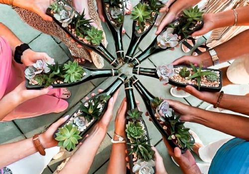 People holding succulent plants in glass bottles arranged in a circular pattern.