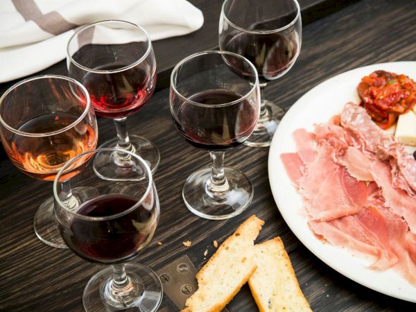 Several wine glasses sit next to a plate of cured meats, cheese, and breadsticks.