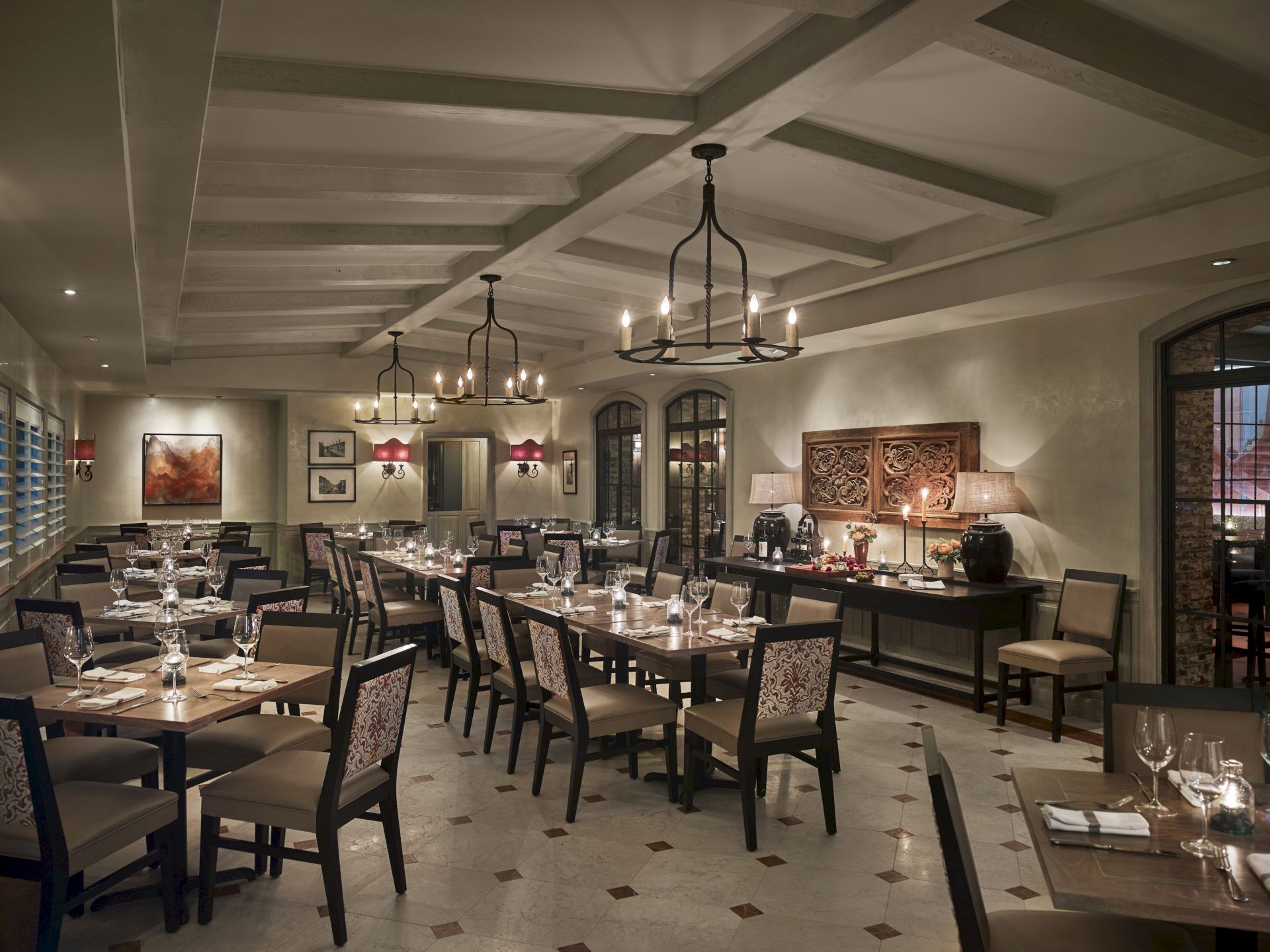 The image shows an elegant restaurant interior with neatly set tables, chandeliers, and stylish decor, creating a warm and inviting atmosphere.