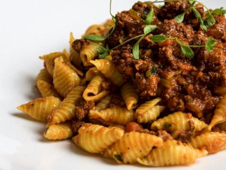 A plate of pasta topped with a rich meat sauce, garnished with fresh herbs, presented on a plain white dish, on a wooden table.