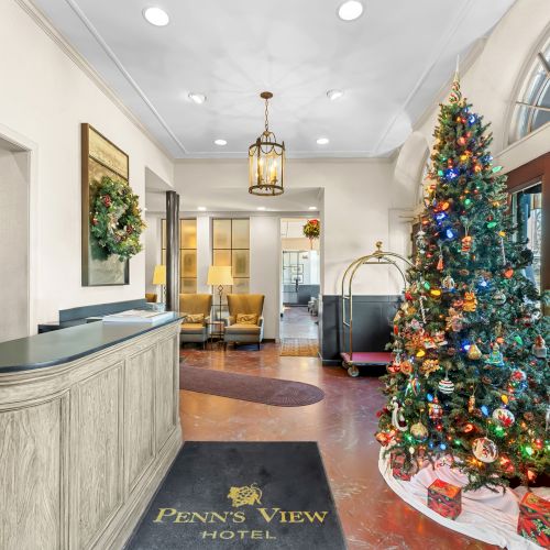 A hotel lobby with a Christmas tree near the entrance, a front desk, seating area, and festive d&eacute;cor in a welcoming hotel reception.