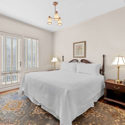 A bright, minimal bedroom with a white bed, light wood furniture, a window with sheer curtains, and soft, neutral decor.