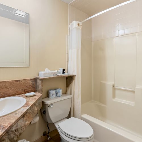 A modern bathroom with a white vanity, round mirror, glass shower enclosure, beige tiled walls and floor, and neutral decor.