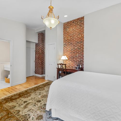A modern bedroom with a vaulted ceiling, white bedding, wooden floors, and a brick fireplace; a cozy, contemporary suite with warm lighting.