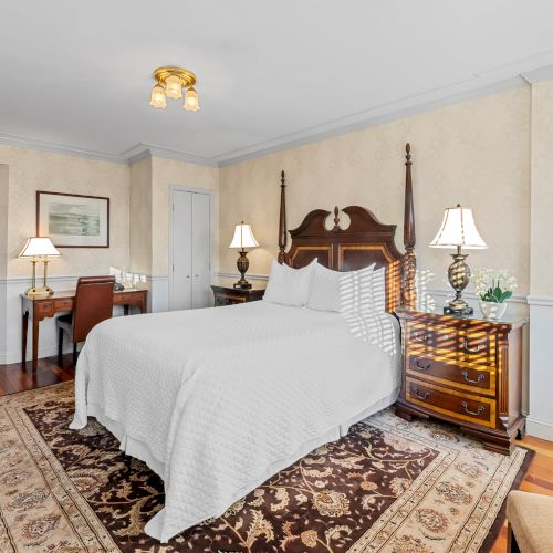 A cozy hotel room with a large bed, nightstands, a chair, and a small seating area; warm lighting and simple decor.