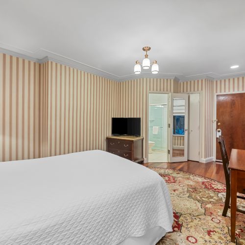 A bright, modern hotel room with two white beds, warm wood furniture, a desk, and a calm, airy feel; window view off to the side.