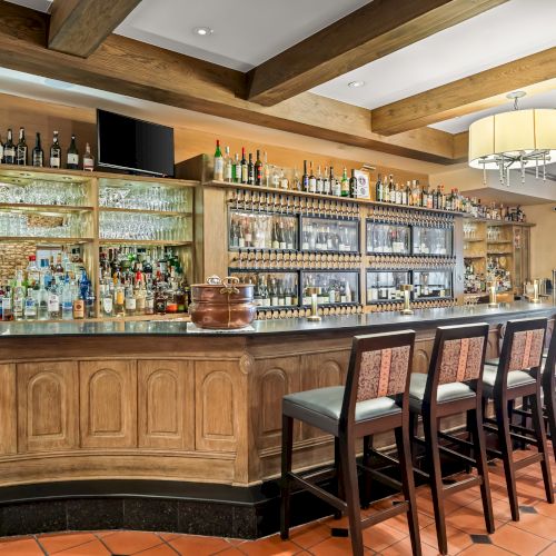 A cozy wooden bar with an array of bottles, a long counter, and high stools, perfect for a relaxing drink at sunset.