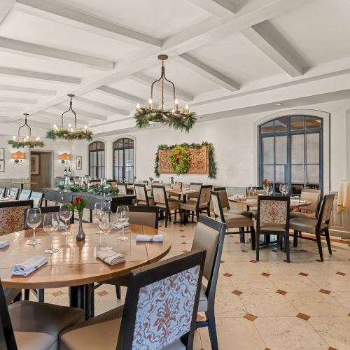 A formal dining room with round tables, tufted chairs, chandeliers, and a buffet area along the back wall.