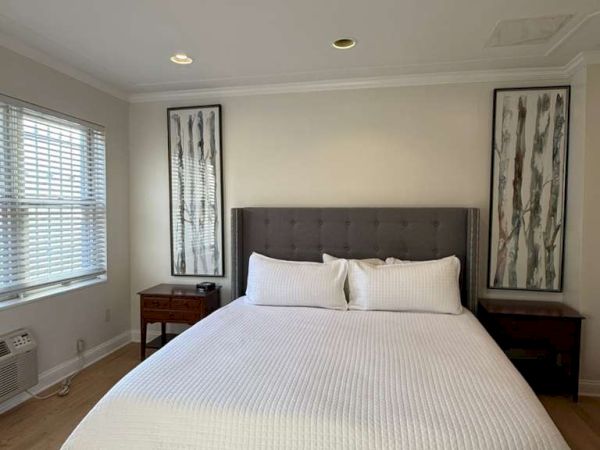 A bright modern bedroom with a king bed, white linens, two nightstands, and framed wall art above the headboard.