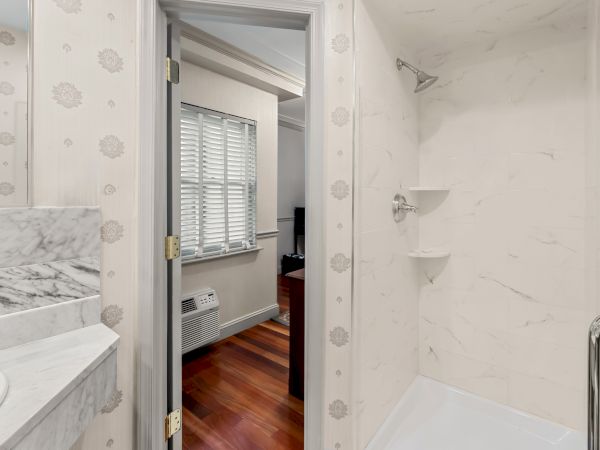 A bright marble bathroom with a toilet, vanity, window blinds, and wall-mounted faucet and shower fixtures.