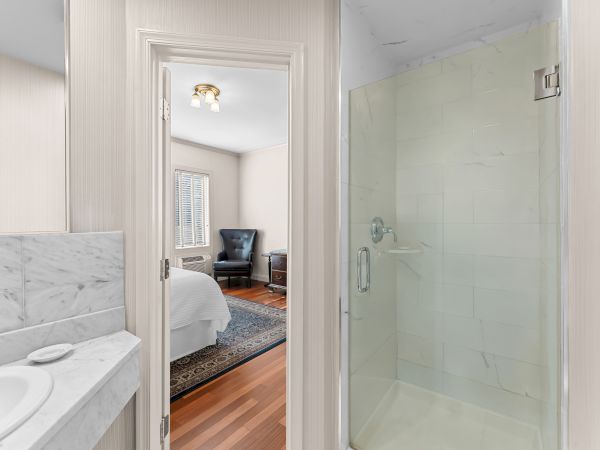 Modern bathroom with marble vanity, open doorway to a sitting area, and a glass shower with chrome fixtures.