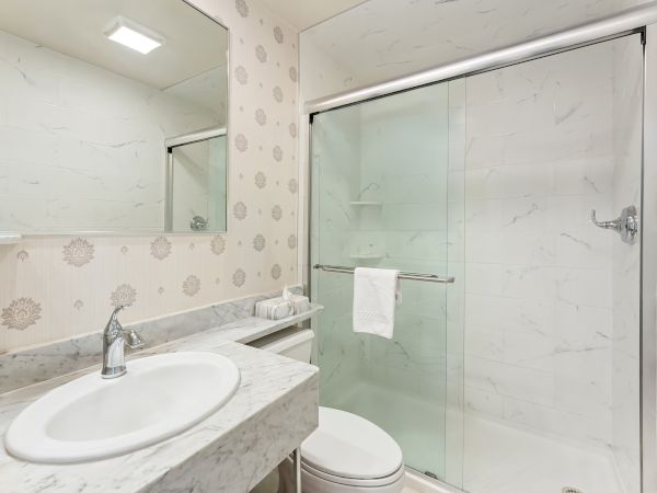 Bright modern bathroom with marble vanity, toilet, and a glass shower enclosure lit by a sleek LED strip.