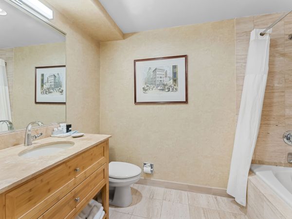A modern bathroom with a marble vanity, toilet, framed artwork, and a rain shower behind white curtains.