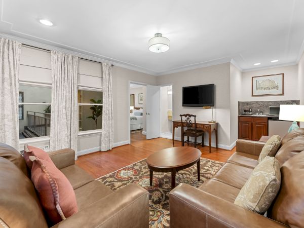 Bright living room with leather sofas, patterned rug, coffee table, TV, curtains, and a small vanity desk.