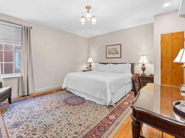 A tidy bedroom with a white bed, bedside lamps, curtains, a patterned rug, and wood doors and dresser.
