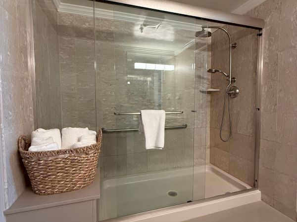A tiled bathroom shower with glass doors, a handheld/rain showerhead, hanging towels, and a woven basket.