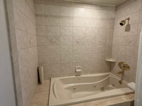 A tiled bathroom with a corner jacuzzi tub, gold faucet, showerhead, and recessed ceiling light.