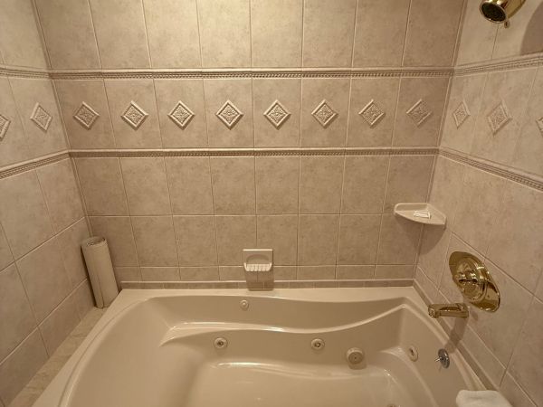 A bathtub in a beige tiled bathroom, with a gold faucet and shower fixtures, and decorative diamond tile accents along the wall.