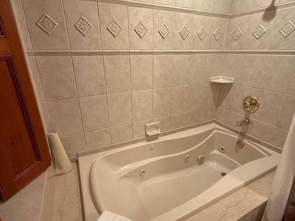 A tiled bathroom with a corner jetted bathtub, matching showerhead faucet, and decorative diamond tile border along the wall.