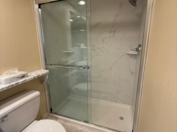 A modern bathroom shower with marble-style tile and glass enclosure, plus a toilet in the foreground.