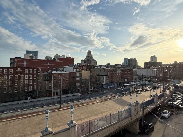 A city skyline at sunset with brick buildings and a tall clock tower under dramatic clouds.